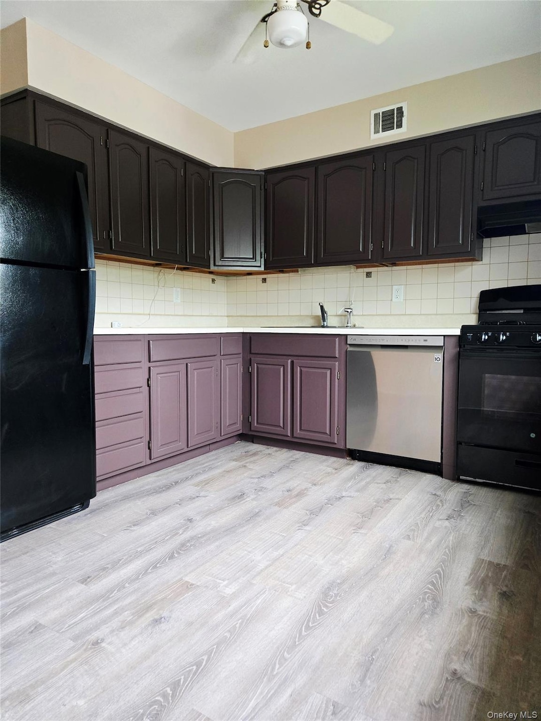 Kitchen with black appliances, light wood finished floors, tasteful backsplash, and under cabinet range hood