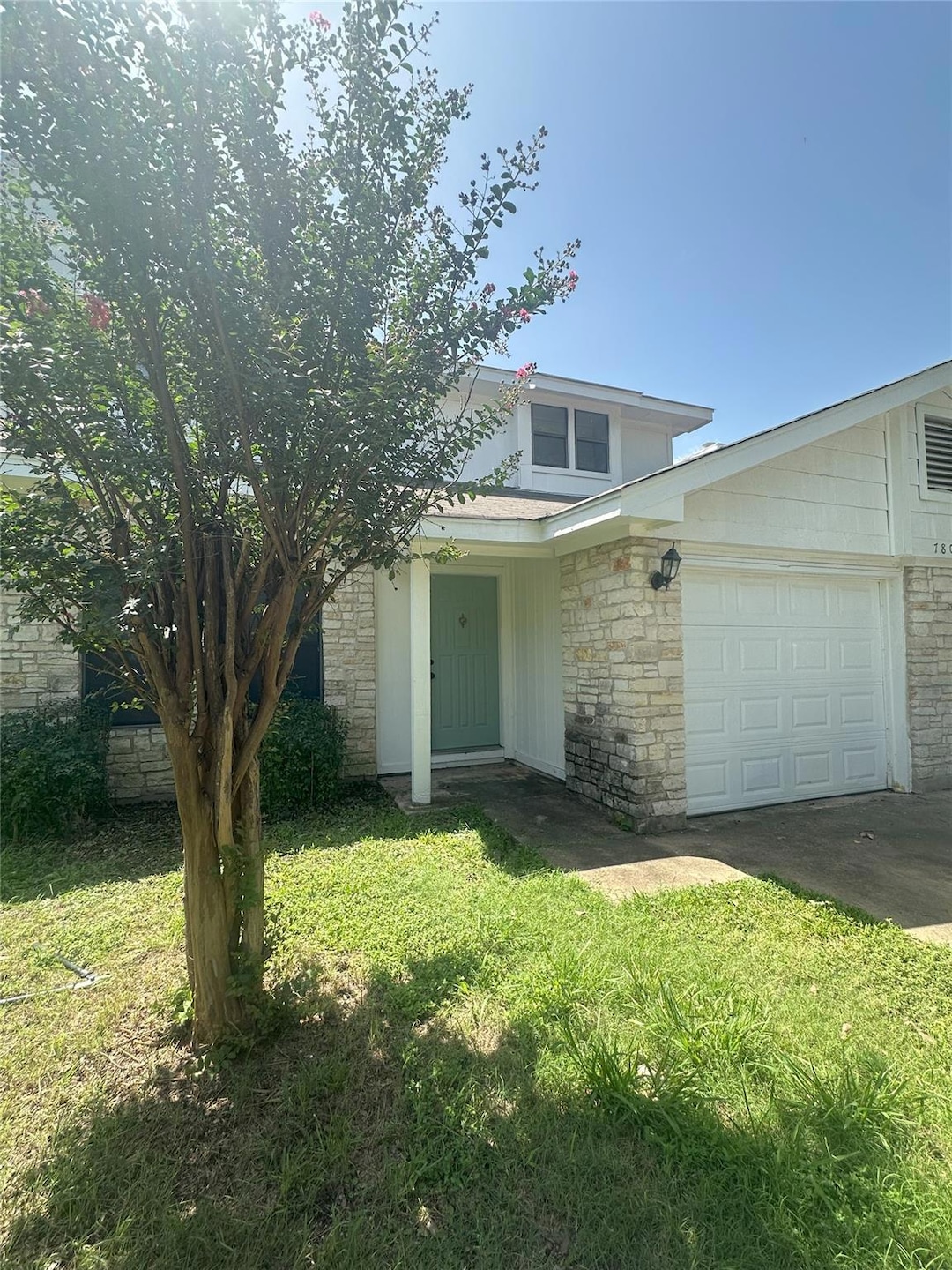 View of front of property featuring a garage, a front lawn, stone siding, and concrete driveway