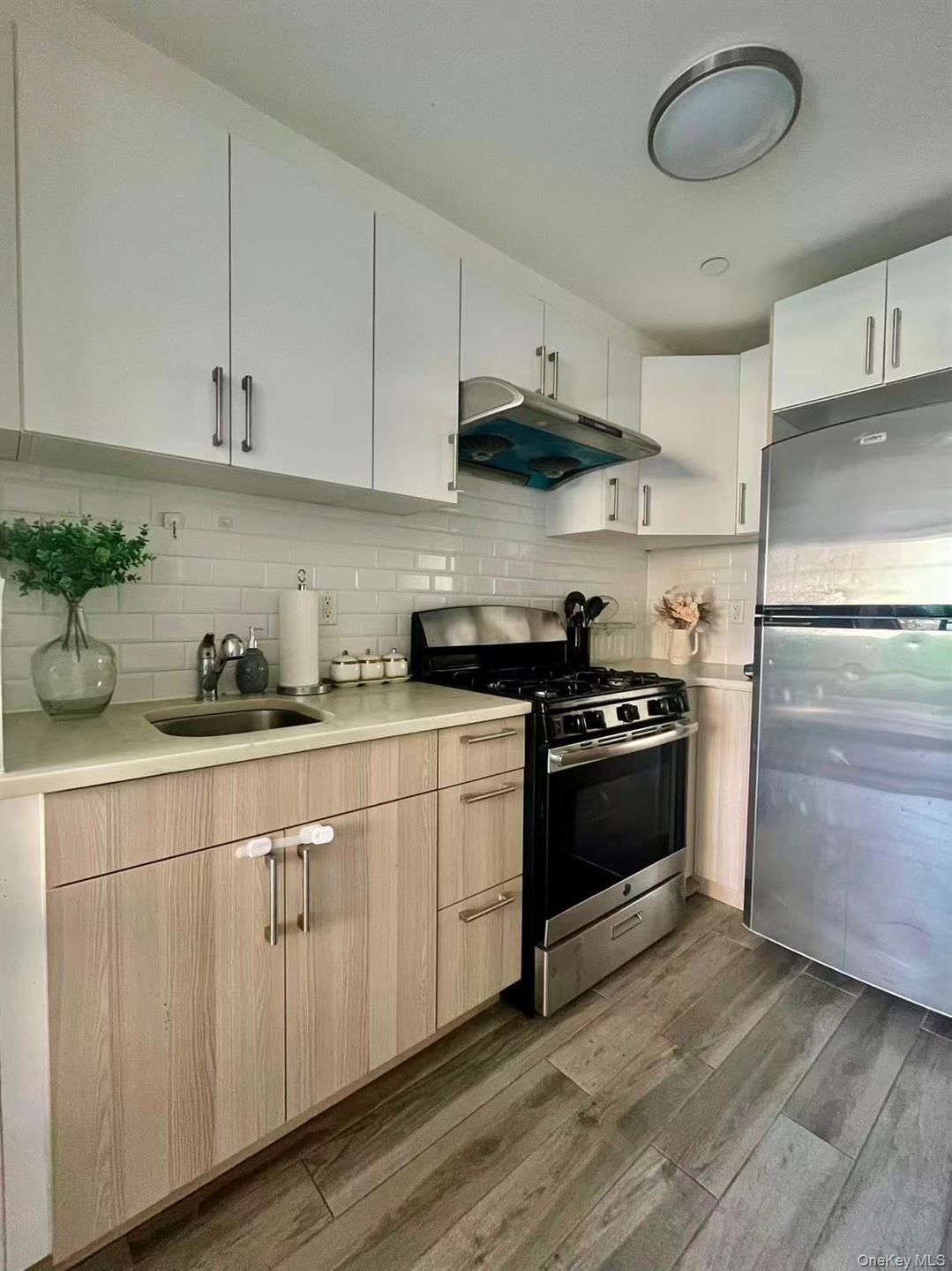 Kitchen featuring stainless steel appliances, range hood, light wood-type flooring, light brown cabinetry, and backsplash