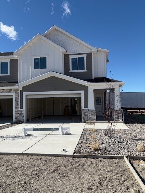 View of front facade with stone siding, board and batten siding, concrete driveway, and a porch