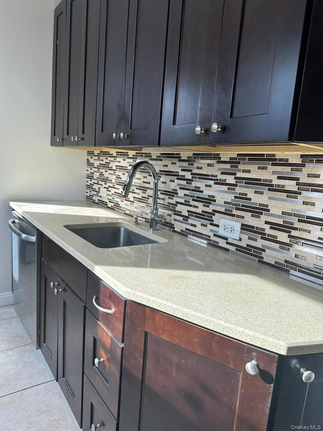 Kitchen featuring light stone countertops, decorative backsplash, dishwasher, and light tile patterned floors
