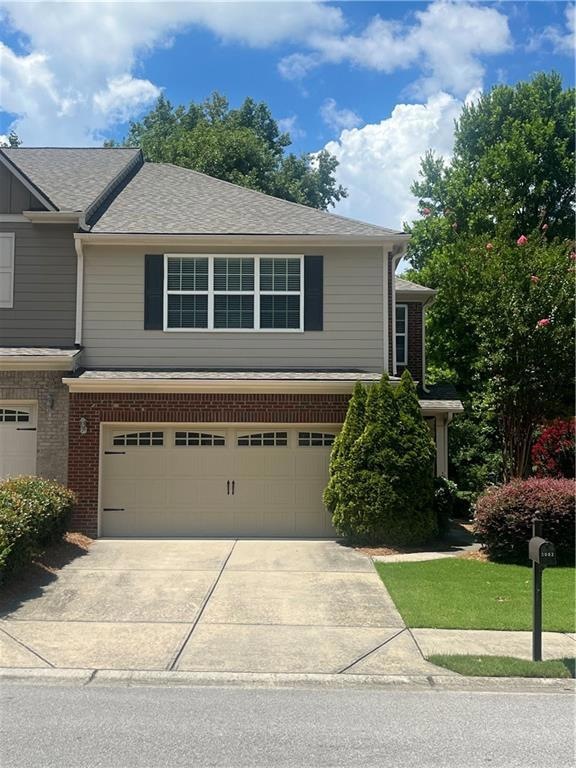 View of front of home featuring a garage, concrete driveway, brick siding, and a shingled roof