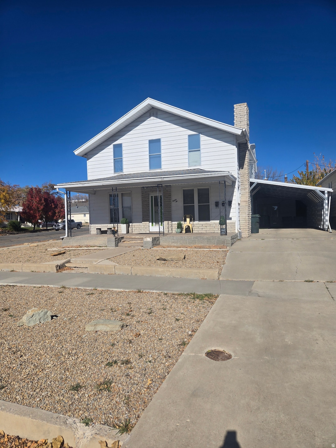 View of front facade featuring a porch, a chimney, and driveway