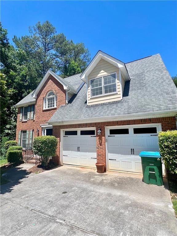 View of front of property featuring brick siding, driveway, and roof with shingles
