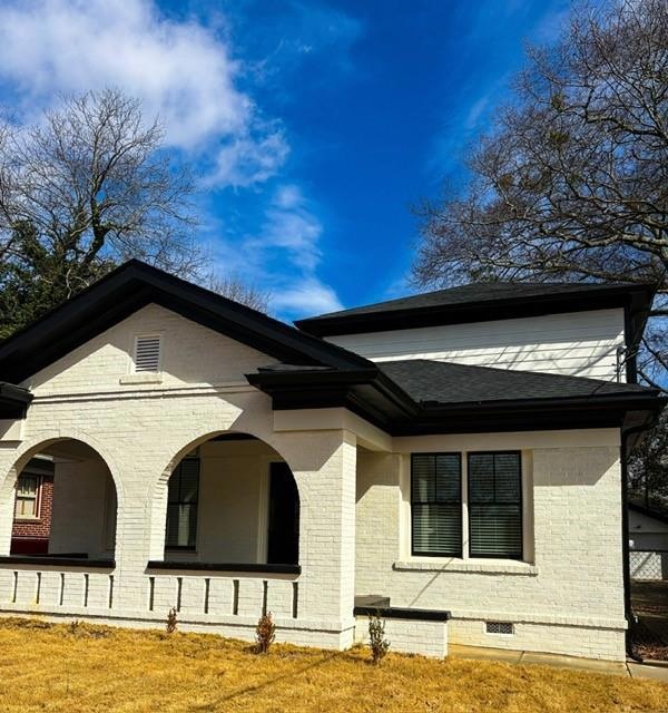 Back of house featuring a shingled roof and brick 