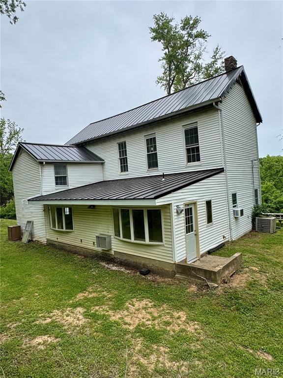 Back of property featuring a chimney, central AC, a yard, and metal roof