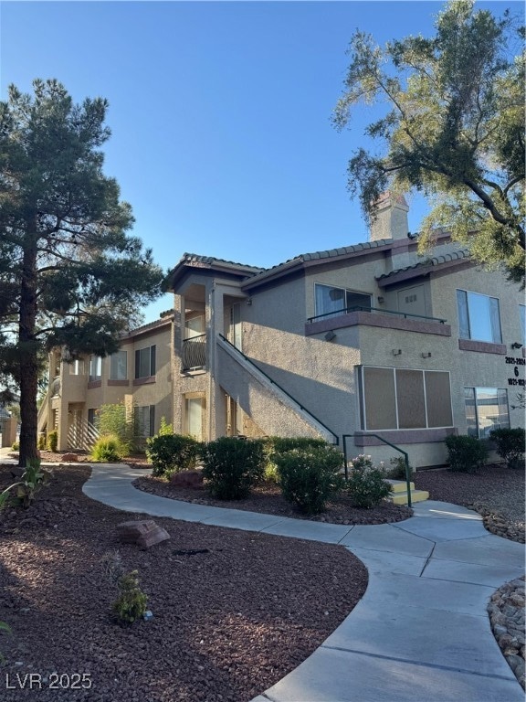 View of side of home featuring a tiled roof, stucco siding, a chimney, and a balcony