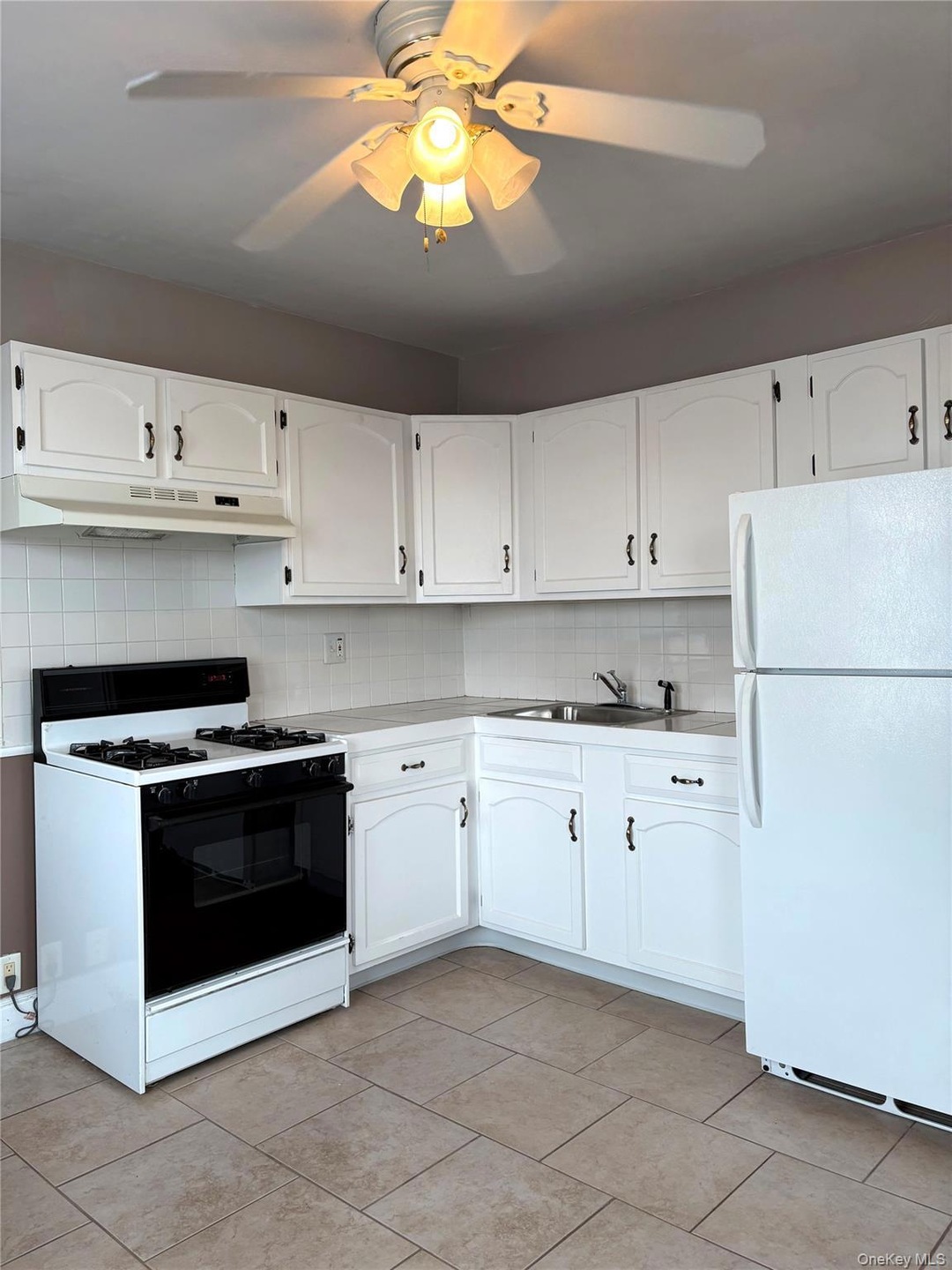 Kitchen with freestanding refrigerator, backsplash, range with gas cooktop, and white cabinetry