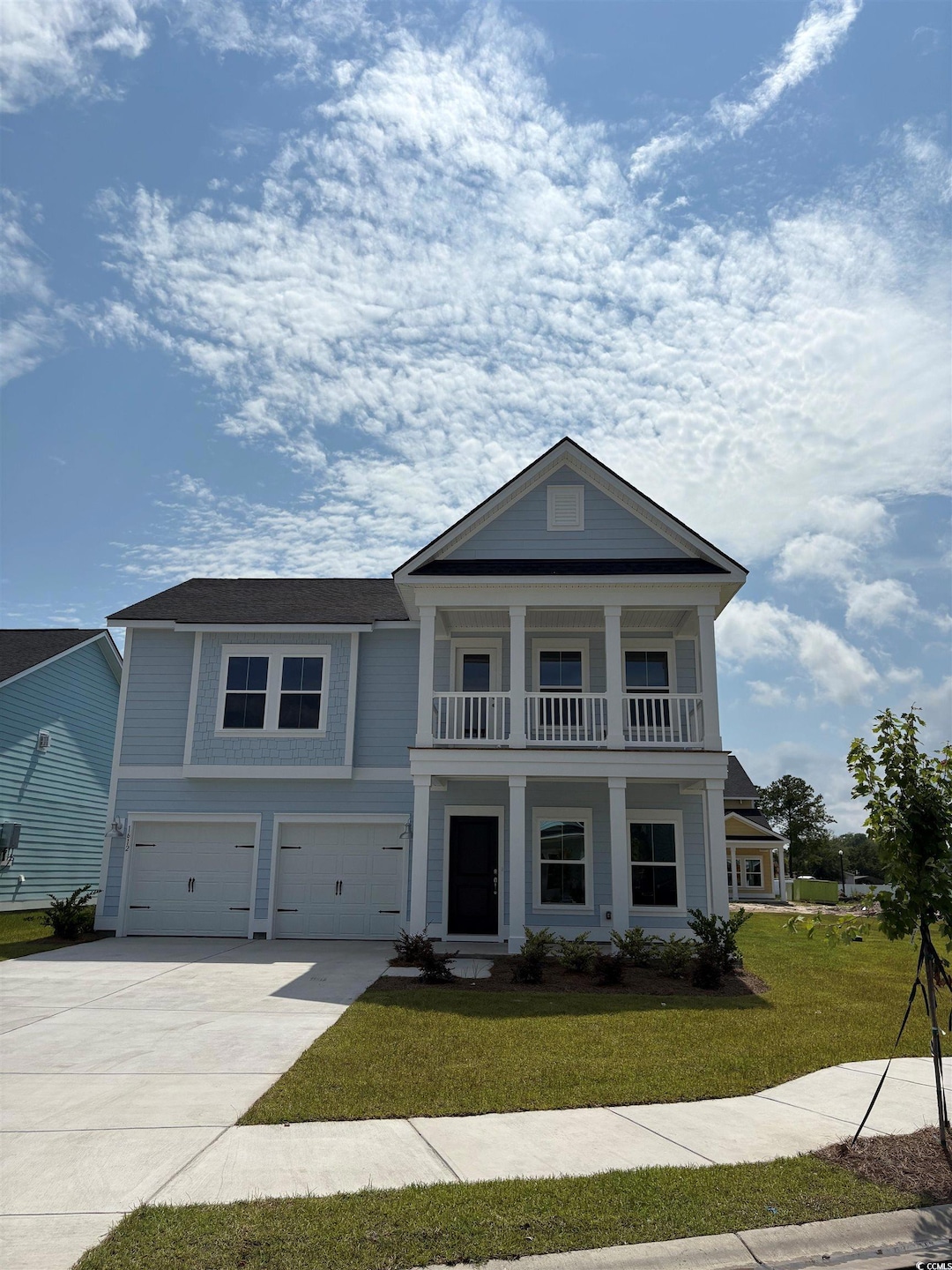 Neoclassical home with a garage, concrete driveway, a front yard, covered porch, and a balcony