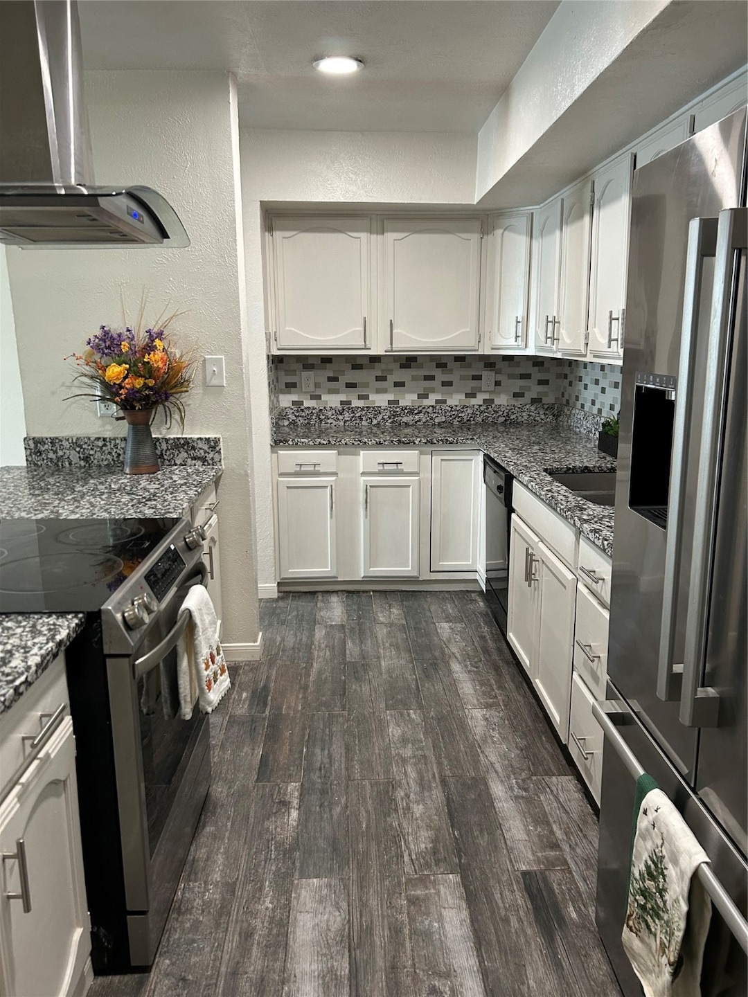 Kitchen featuring stove, a textured wall, decorative backsplash, dark stone countertops, and ventilation hood