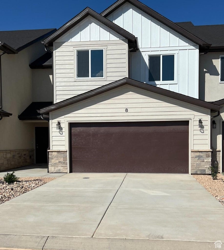 View of front facade featuring stone siding, a garage, driveway, and board and batten siding