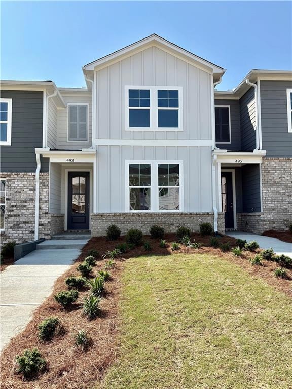 View of front of home featuring board and batten siding, a front lawn, and brick siding