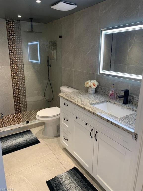 Full bath with tile walls, vanity, walk in shower, and light tile patterned floors