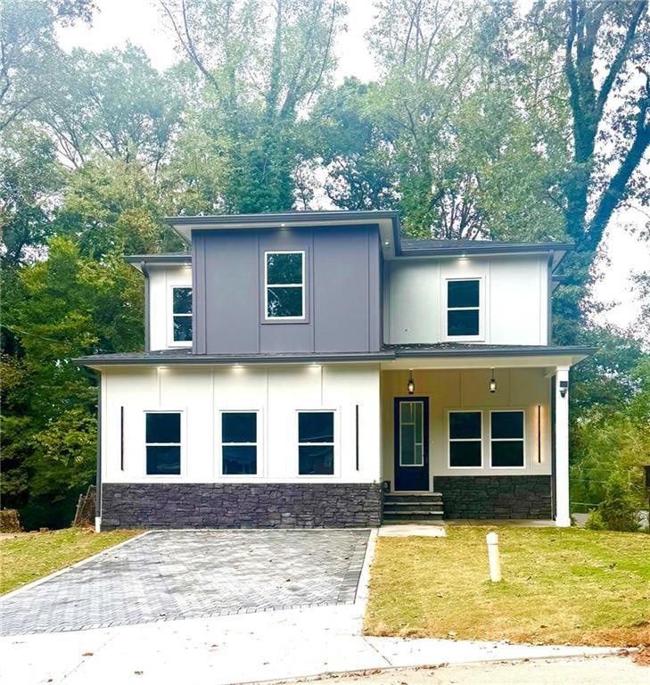 Modern home with stone siding, covered porch, stucco siding, and a front lawn