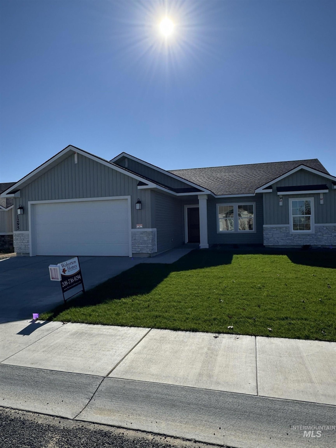 Single story home featuring board and batten siding, stone siding, a front yard, an attached garage, and concrete driveway