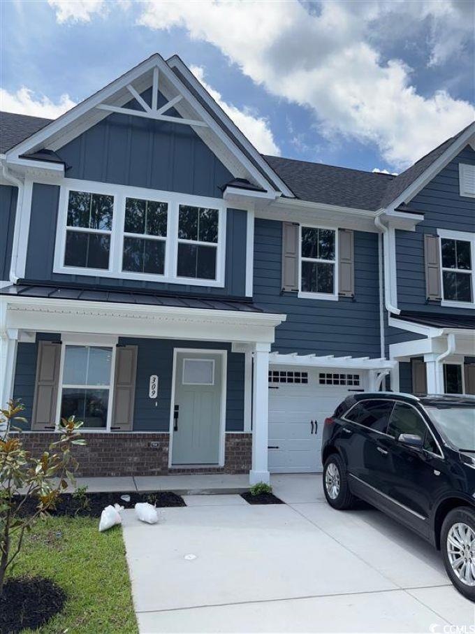View of front of property featuring an attached garage, concrete driveway, a porch, brick siding, and board and batten siding