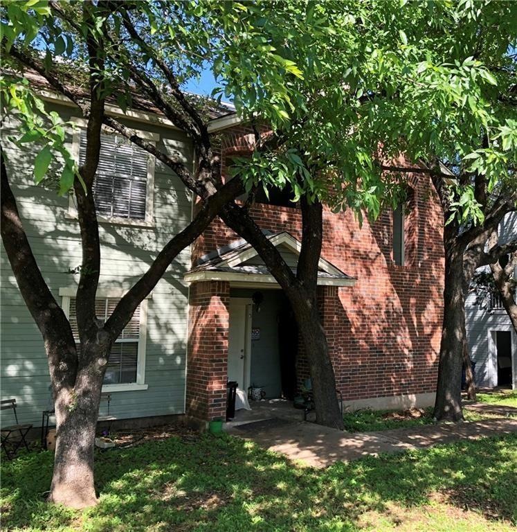 View of property hidden behind natural elements featuring a front lawn and brick siding
