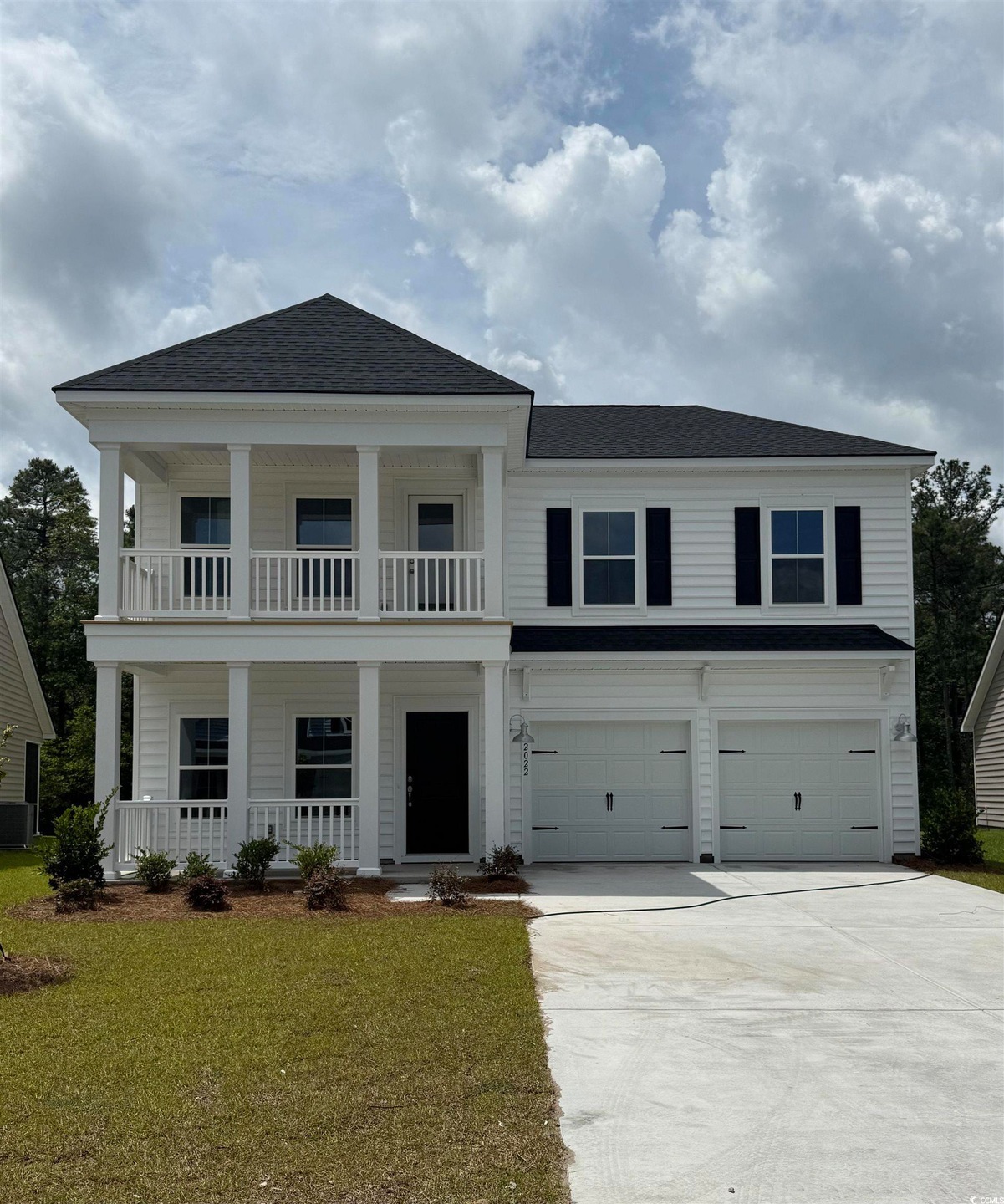 Greek revival house featuring covered porch, an attached garage, concrete driveway, a front lawn, and a balcony