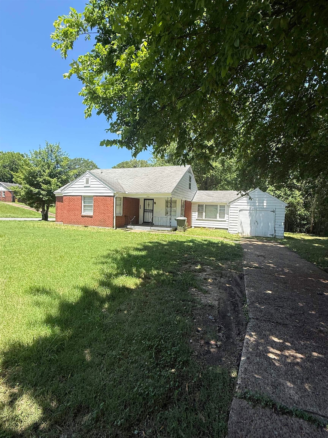 Ranch-style house with a porch, asphalt driveway, a front yard, an attached garage, and an outbuilding