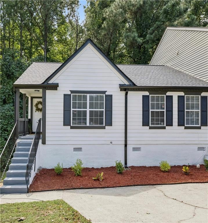 View of front of property with crawl space, a shingled roof, stairs, and a porch
