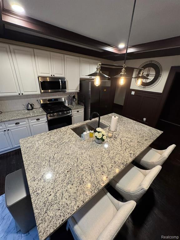 Kitchen with a breakfast bar area, light stone countertops, appliances with stainless steel finishes, white cabinetry, and decorative light fixtures