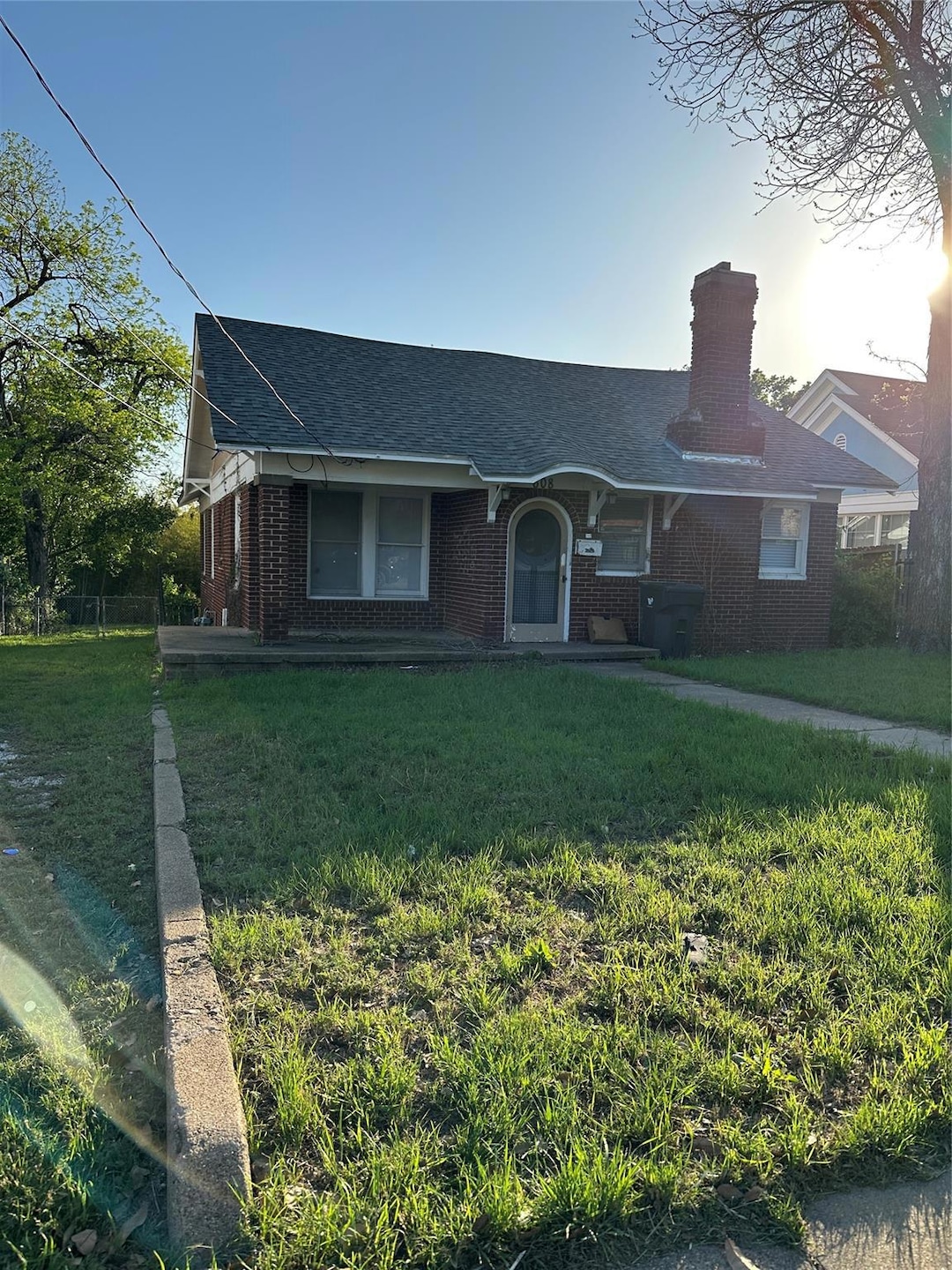 View of front facade with roof with shingles, a chimney, a front yard, and brick siding