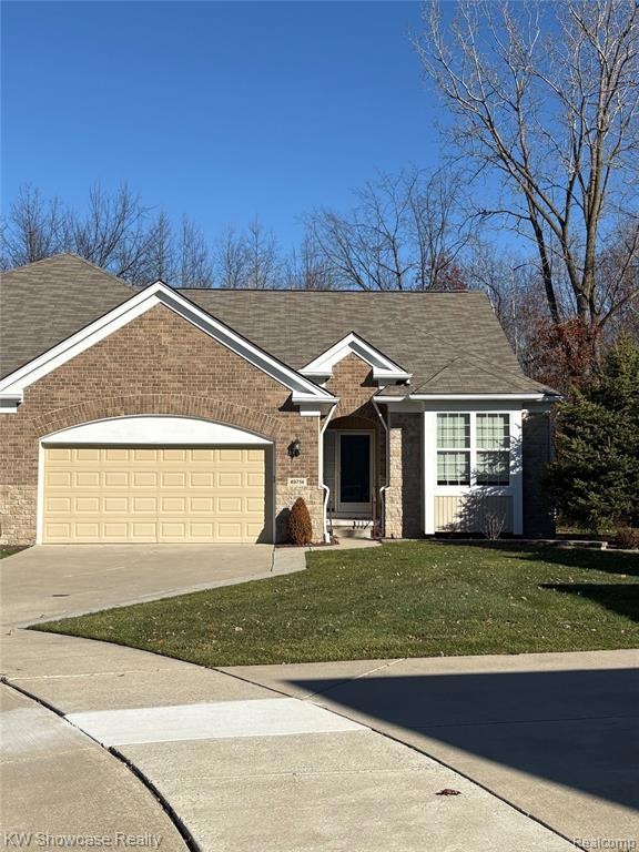 Ranch-style home with a front lawn, driveway, a shingled roof, a garage, and brick siding