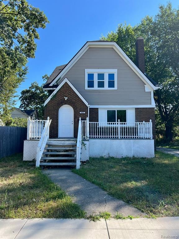 View of front of property featuring brick siding, a front yard, and a chimney