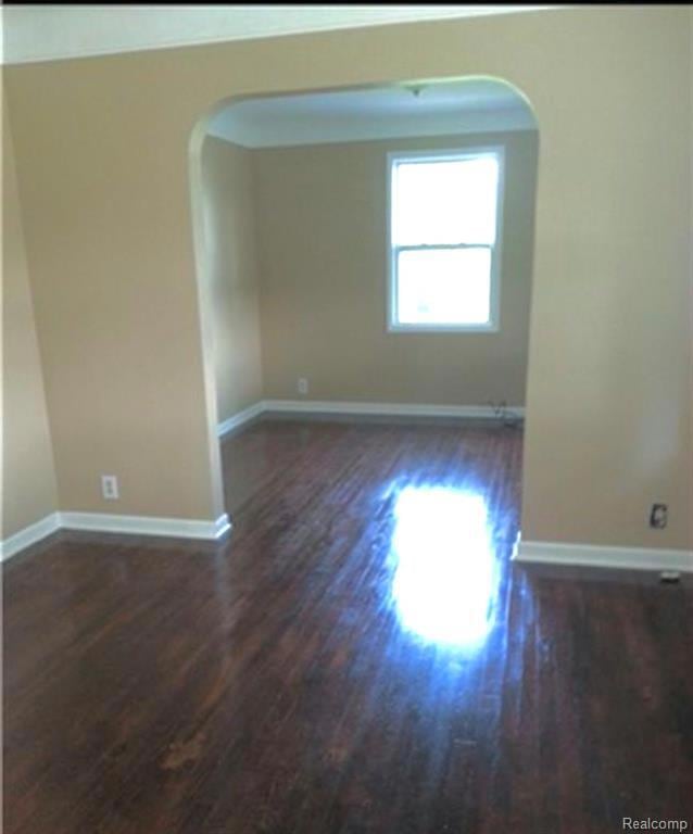 Spare room with arched walkways and dark wood-style floors