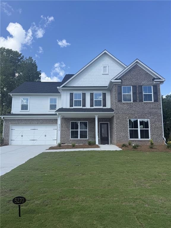 View of front of home featuring a garage, concrete driveway, a front yard, and brick siding