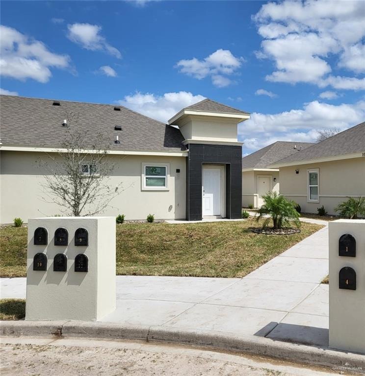 View of front facade featuring stucco siding, a front yard, and a shingled roof