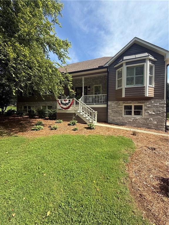 View of front of house featuring stone siding, a porch, a front yard, and a shingled roof