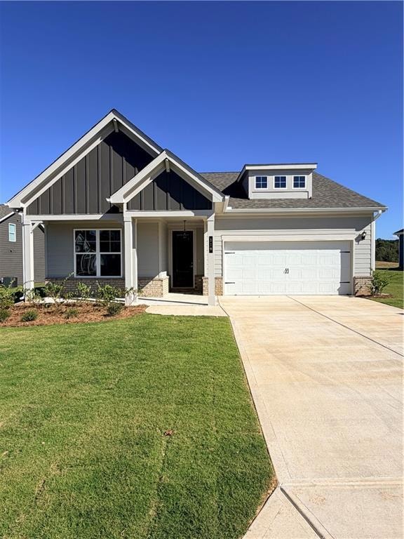 Craftsman inspired home featuring a shingled roof, concrete driveway, covered porch, a front yard, and board and batten siding