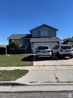 Split level home featuring concrete driveway, an attached garage, and a front lawn