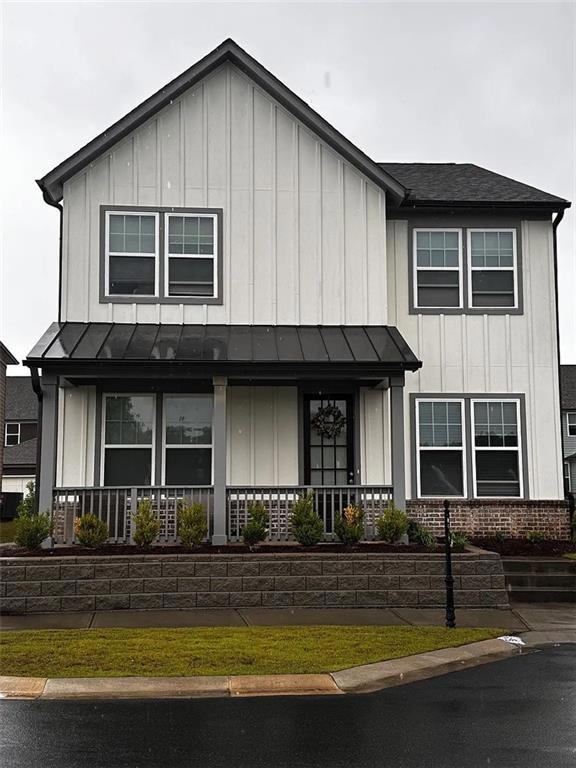 View of front of property featuring board and batten siding, a porch, a standing seam roof, and brick siding