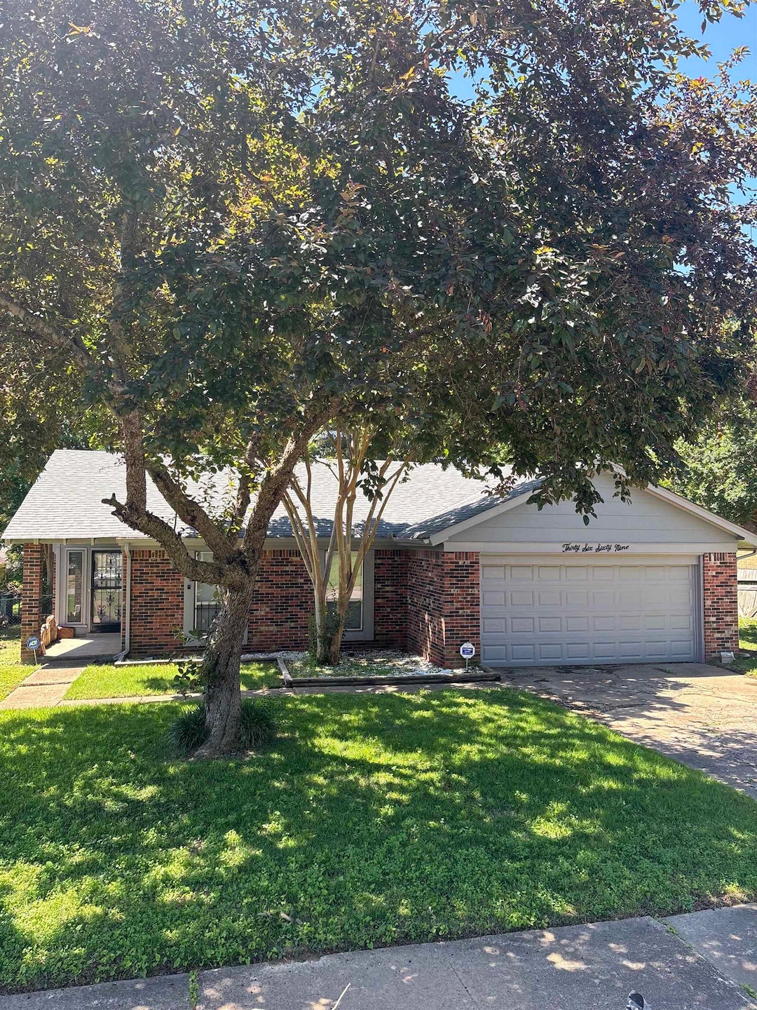 View of front of property featuring a front lawn, brick siding, driveway, and an attached garage
