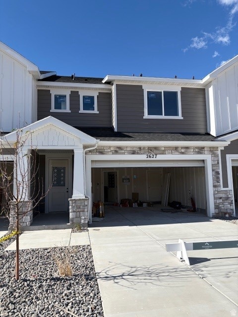 View of front facade featuring stone siding, concrete driveway, board and batten siding, and an attached garage