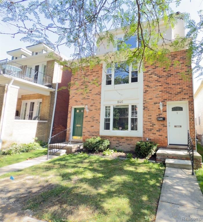 View of front of property with a balcony, a front yard, and brick siding