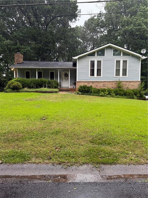 View of front of property with brick siding, a chimney, and a front yard