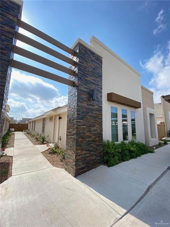 View of property exterior featuring stucco siding, a pergola, and stone siding