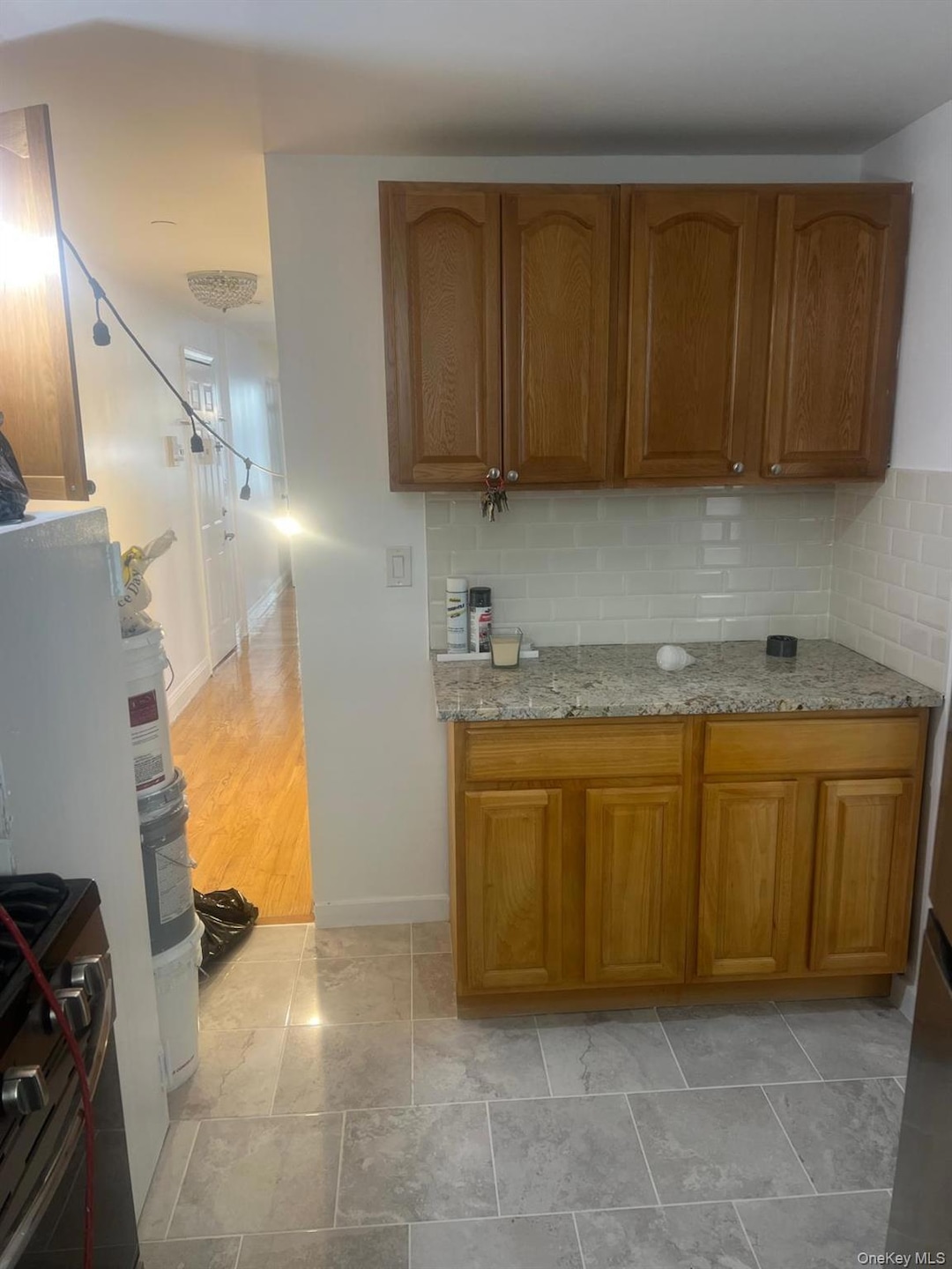 Kitchen featuring light stone counters, brown cabinetry, tasteful backsplash, and stainless steel gas stove