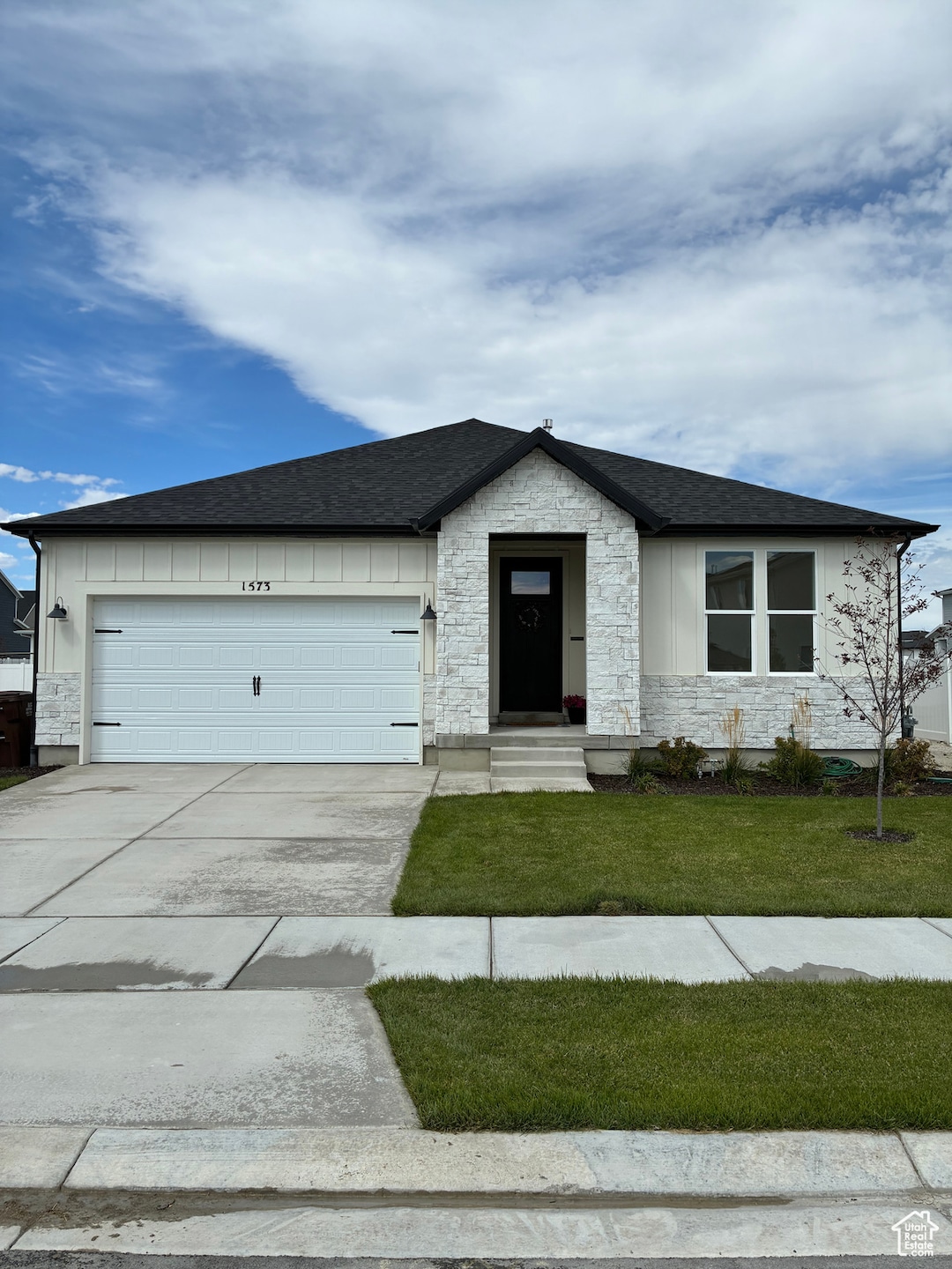 View of front of home with stone siding, driveway, a shingled roof, a garage, and a front yard