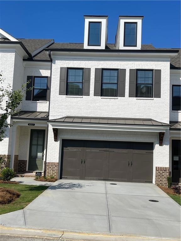 View of front of property featuring brick siding, a garage, concrete driveway, a standing seam roof, and a metal roof