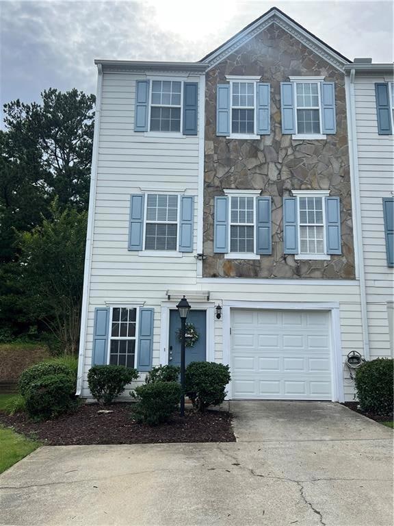 Townhome / multi-family property with stone siding, driveway, and a garage