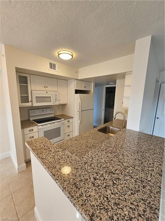 Kitchen featuring light stone countertops, stove, freestanding refrigerator, light tile patterned floors, and a textured ceiling