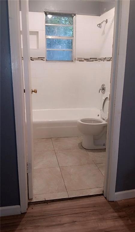 Bathroom with tiled shower / bath, hardwood / wood-style floors, and toilet