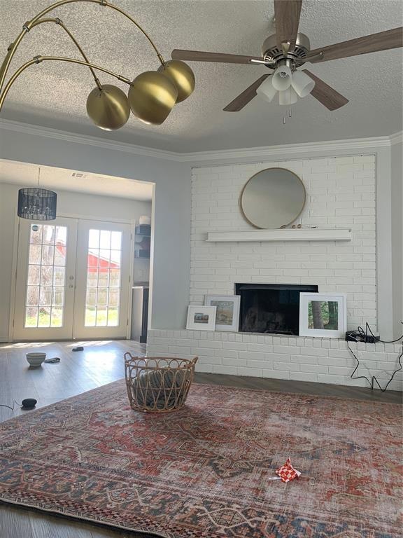 Living room with crown molding, a textured ceiling, french doors, ceiling fan, and a fireplace