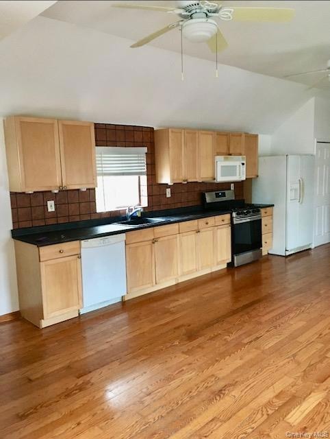 Kitchen featuring light brown cabinetry, a ceiling fan, white appliances, and vaulted ceiling