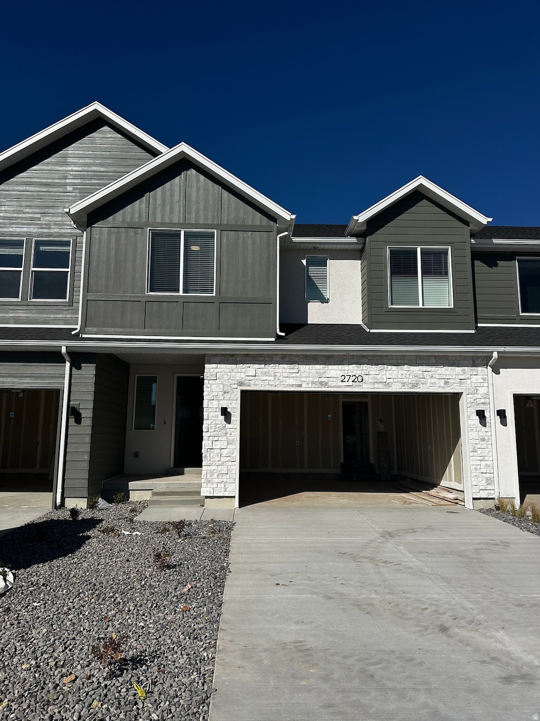 View of front facade with stone siding, a garage, concrete driveway, a porch, and board and batten siding