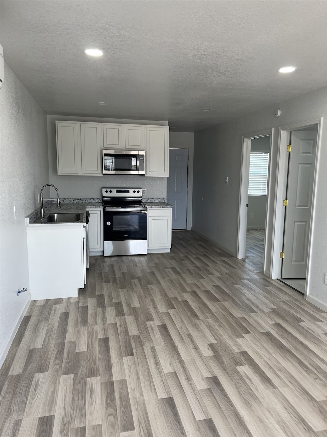 Kitchen featuring white cabinetry, appliances with stainless steel finishes, light wood-type flooring, a textured ceiling, and open floor plan